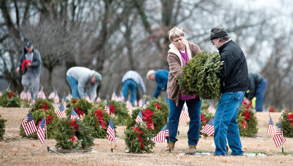 Volunteers remove the holiday wreaths from soldiers’ graves at Woodland Cemetery on Saturday. The greenery was placed in December as part of Wreaths Across America.