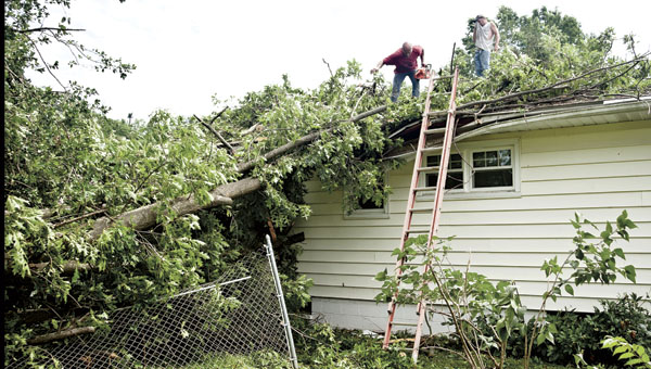 THE TRIBUNE/JESSICA ST JAMES Volunteers help out a neighbor as they remove a tree from the top of a home outside of Chesapeake Wednesday.