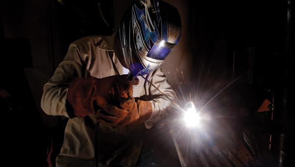 A ball of white light illuminates from the end of a welding torch while students practice welding techniques.
