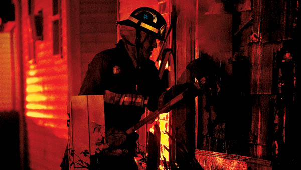 THE TRIBUNE/JESSICA ST JAMES Ironton Fire Fighter Jack Delong uses an ax as he battles a house fire on the 1900 block of South Second Street early Thursday morning. The fire was reported after 5 a.m. and was fully engulfed. The home is a total loss.