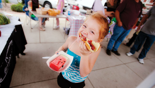 Six-year-old Joshline Sanford bites into her hot dog while at the Ironton Farmers Market on Saturday. This week Ironton in Bloom hosted a cookout with hot dogs and watermelon.