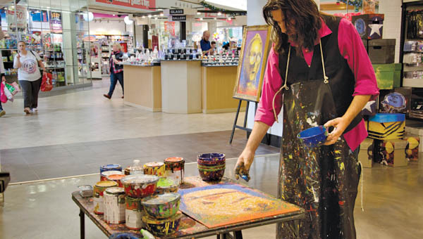 Artist Billy Tackett works on a painting of on Friday at the entrance of The Inner Geek comic shop in the Ashland Town Center.