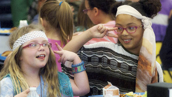 Hannah Gillum, left, and Kyra Taylor, right, is feeling groovy as they eat their lunch Tuesday and dance to the music at South Point Elementary. Students and faculty were encouraged to dress up in a groovy fashion for the book fair themed “Feeling Groovy About Books.”