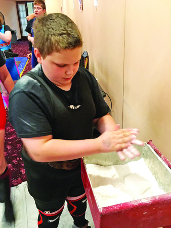Ironton Middle School seventh grade student Bryce Maynard applies chalk to keep his hands dry for his lift in the WNPF World Championships. Maynard finished first as he set two world records en route to winning a world title. (Photo Submitted)